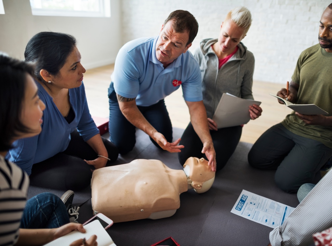 First aid training course — instructor demonstrating CPR to a group of workplace delegates